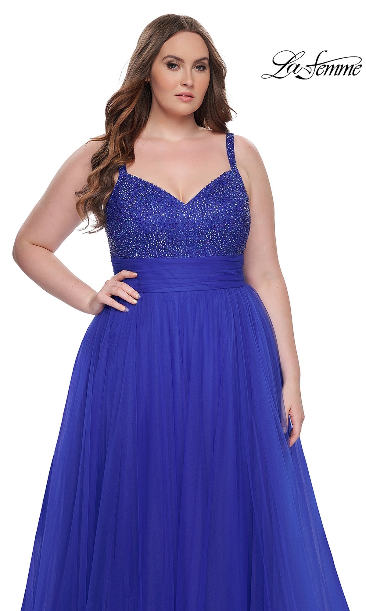 A woman models the La Femme Long Prom Dress 31251 in royal blue, featuring a beaded bodice and tulle skirt, standing against a plain white background with the La Femme logo in the top right corner.